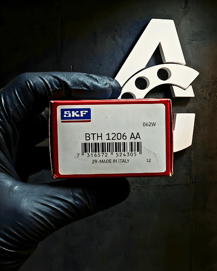 Mano con guante negro sosteniendo una caja SKF con la referencia BTH 1206 AA frente al isotipo de Arcaragua Group